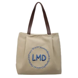 Minimalist canvas tote bag with LMD blue embroidery and brown leather handles on white background