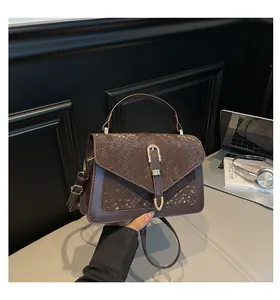 Detail of a brown-purple handbag featuring snake-embossed flap and gold metal buckle