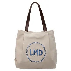Minimalist canvas tote bag with blue floral embroidery and leather handles on white background