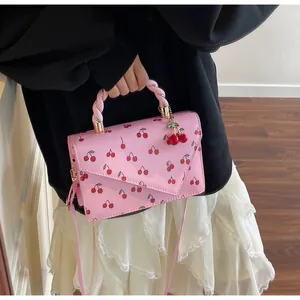 Détail d'un sac bandoulière rose avec motifs cerises et un charmant pendentif cerise
