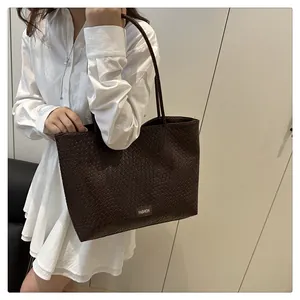 Détail du grand sac cabas marron foncé à texture tressée porté à l'épaule sur modèle