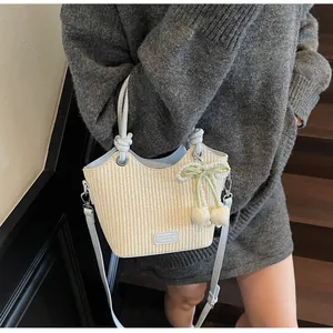 Detalle de bolso cubo de paja con correas de cuero azul y colgante de lazo y perla