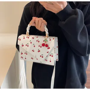 Détail du sac bandoulière blanc avec imprimé cerises et poignée tissée sur modèle