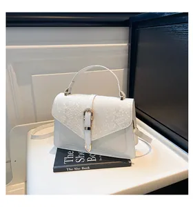 Close-up of white crossbody bag with snake skin embossed flap and gold metal buckle