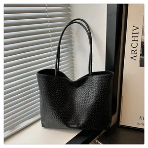 Détail d'un sac cabas noir à texture tressée avec étiquette mode et longues bandoulières