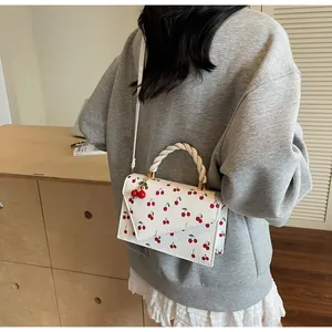 Détail du sac bandoulière blanc avec imprimé cerise et poignée tressée sur modèle