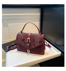 Close-up of burgundy flap bag with snake pattern texture and gold buckle detail