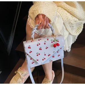 Détail d'un sac à main doux à motif cerises avec poignée tressée et bandoulière réglable