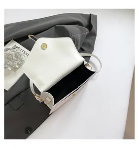 Detail view of white envelope bag featuring gold magnetic clasp and black lining texture