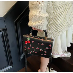 Détail du sac à main noir à imprimé cerise avec un pendentif cerise porté par un modèle