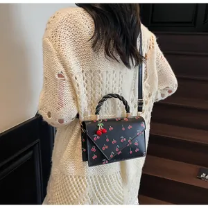 Détail du sac bandoulière à imprimé cerise avec rabat asymétrique et poignée tressée