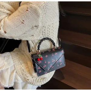 Détail d'un sac à main noir avec imprimé cerise et poignée torsadée porté par un mannequin