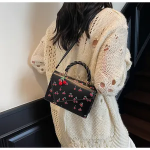 Détail du sac à bandoulière noir à motif cerise avec poignée tressée et pendentif