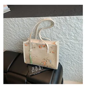 Detail of beige embroidered tote bag with floral motifs and elegant green tassel charm