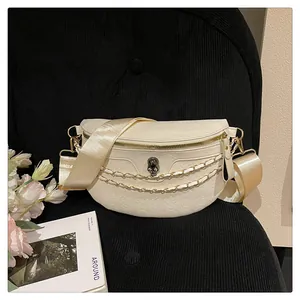 Detail of cream crossbody bag with skull embossing, gold chain, and wide shoulder strap