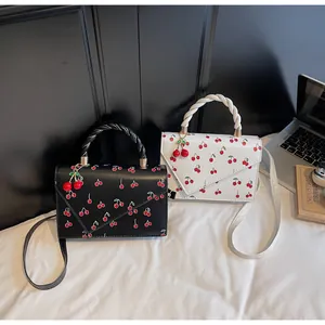 Détail du motif cerise et du pendentif cerise sur des sacs à main blanc et noir chic