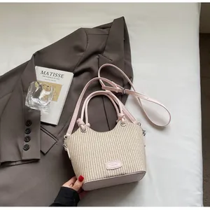 Detalle del bolso tipo cubo de paja con ribete de cuero rosa y placa de logo