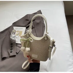 Detalle del bolso tipo cubo de paja con ribete de cuero blanco y colgantes de tulipán y perla