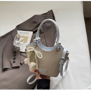 Detalle del bolso tipo cubo de paja con asa de cuero azul y colgante de lazo de perlas