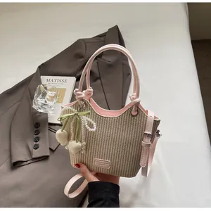 Detalle del bolso de paja tipo cubo con ribete de cuero rosa y colgante de perlas y lazo
