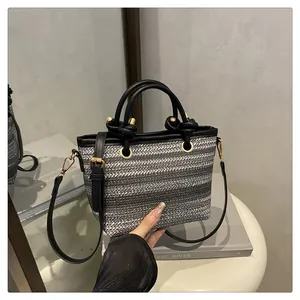 Detail of woven silver and black tote featuring leather handle and gold hardware