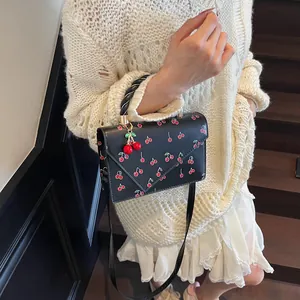Sweet black handbag with cherry patterns and decorative pendant shown on a model