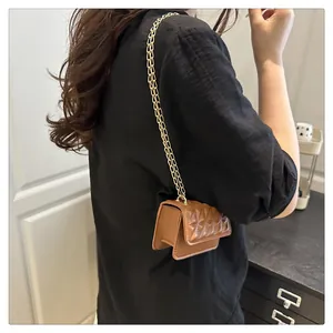 Detail of a dark brown mini quilted crossbody bag with a gold chain strap on a model