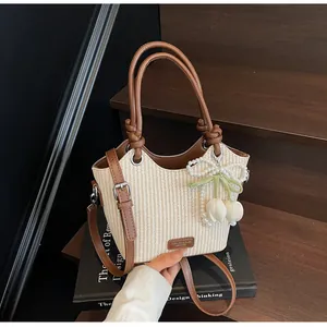 Detalle del bolso tipo cubo de paja con colgantes de tulipán y asa de cuero