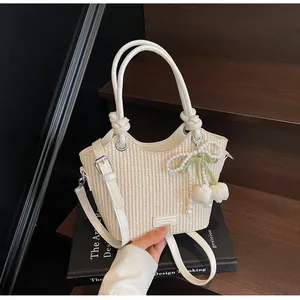 Detalle del bolso de paja crema con asas de cuero y colgante de tulipán y perlas