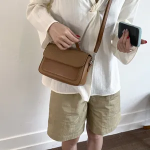 Detail of a brown crossbody bag featuring a woven textured flap and adjustable strap