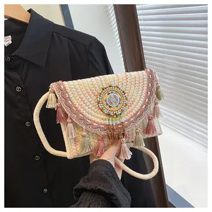 Dettaglio della borsa a busta in paglia intrecciata con ricami colorati e nappe