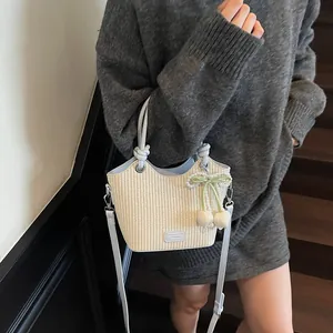 Bolso cubo de paja con ribete de cuero azul y colgante de lazo de perlas en escenario