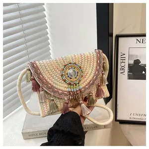Dettaglio della borsa a tracolla in paglia intrecciata con ricami boho e nappe colorate