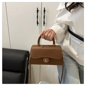 Detail of caramel leather handbag featuring a vintage gold round lock and smooth flap texture