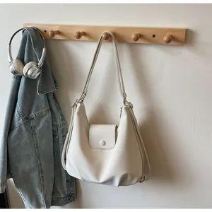 Detail of minimalist cream PU leather shoulder bag with decorative round buckle and dual straps