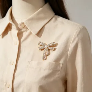 Detail of elegant gold bow brooch with crystals and pearl on a beige shirt