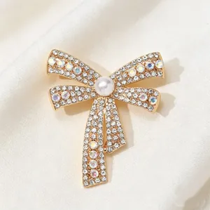 Elegant bow-shaped brooch with golden finish, white pearl and sparkling crystals