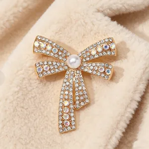 Close-up of bow brooch with colorful rhinestones and pearl on beige fabric