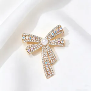 Elegant gold bow brooch with sparkling crystals and a pearl on white silk background