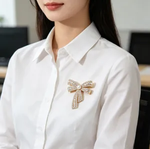 Detail of elegant gold bow brooch with rhinestones and pearl on white shirt