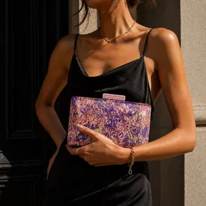 Detail of marble pattern acrylic evening bag with gold chain strap on a black satin dress