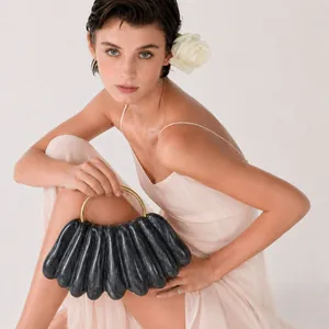 Close-up of a dark grey wavy acrylic evening clutch bag with a gold round handle