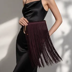 Sac à bandoulière bordeaux à franges et cadre doré, porté sur une robe noire chic