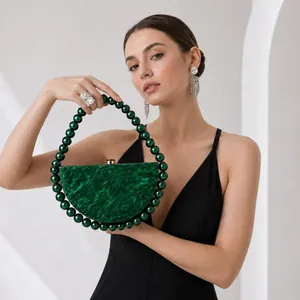 Detail of dark green acrylic clutch bag with round beaded handle and gold metal clasp