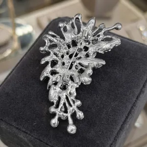 Irregular cutout silver metal brooch back view with secure safety pin on velvet