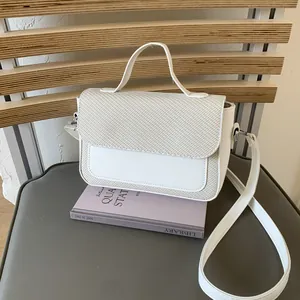 Detail of off-white crossbody bag with woven texture on a wooden bench setting
