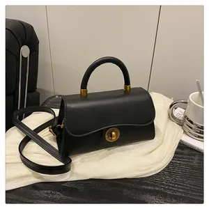 Detail of black leather handbag featuring a golden round swivel lock and single top handle