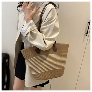 Detail view of woven straw tote bag featuring brown leather straps and striped pattern