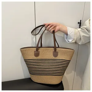 Detailed view of woven straw tote bag featuring black stripes and leather handles
