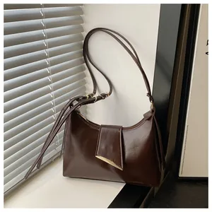 Detail of dark brown polished leather hobo bag with gold metal edge on flap cover